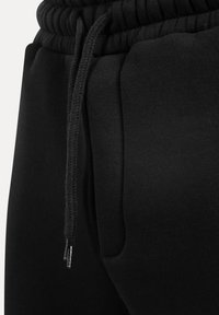 Sorte sweatpants med en elastisk talje med snoretræk, sidelommer og en glat, tekstureret stoffinish.