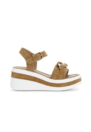 Sandalo platform in suede marrone con suola bianca, dotato di una fascetta alla caviglia e dettaglio annodato nella parte anteriore. Chiusura con fibbia laterale.