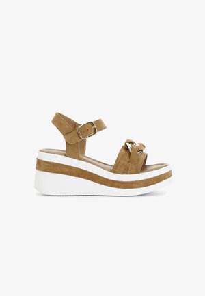 Bruine suede platform sandaal met een witte zool, voorzien van een enkelband en een geknoopt voordetail. Gespsluiting aan de zijkant.