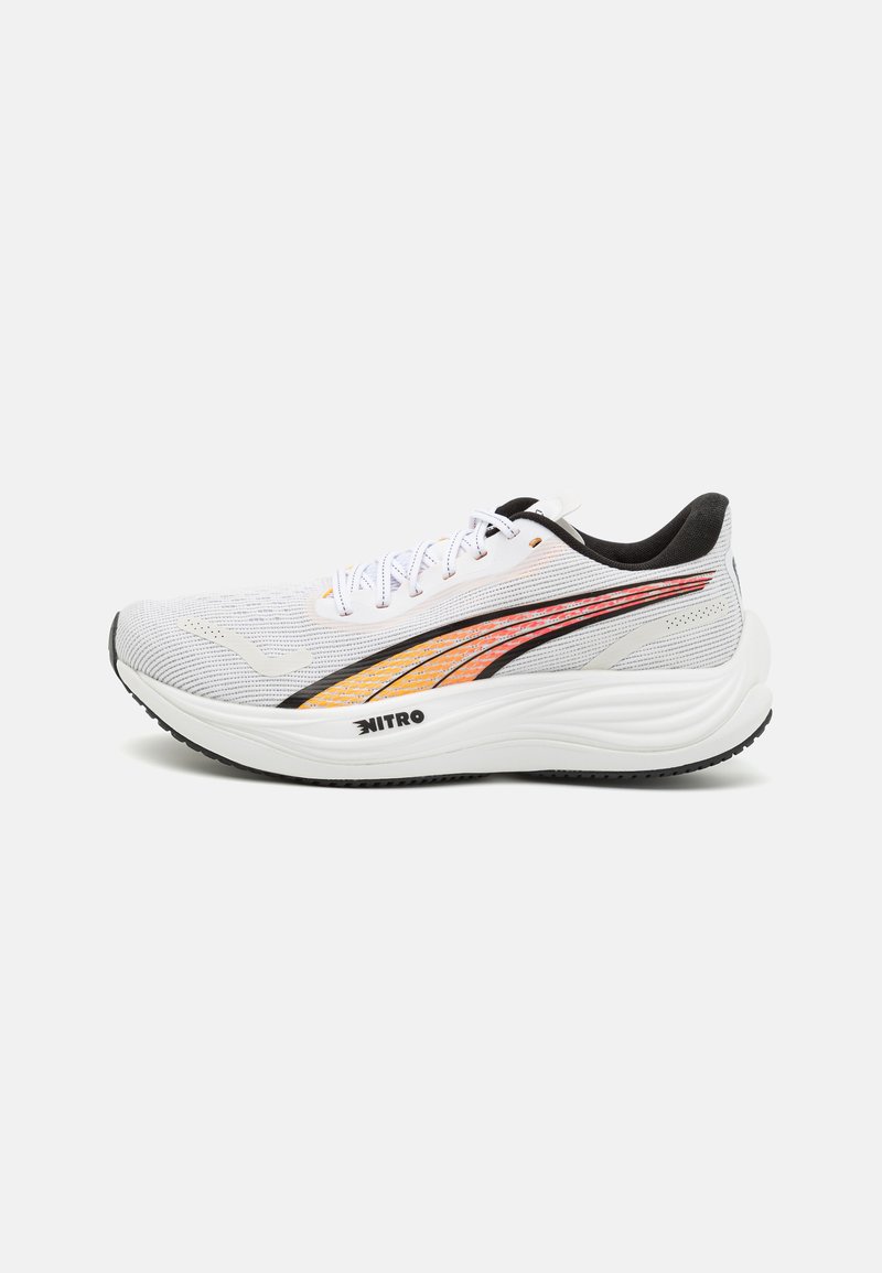 Zapato deportivo blanco con una parte superior texturizada, acentos en naranja y negro. Presenta una suela curved y el logo "NITRO" en el costado.