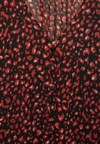 Tissu noir avec des taches de léopard irrégulières rouges et blanches, avec une rangée verticale de boutons ronds recouverts de tissu.