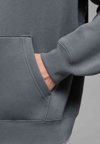 Felpa grigia con tasca a marsupio, polsini e orlo a costine. Realizzata in un tessuto morbido e dalla trama liscia, adatta per un abbigliamento casual.