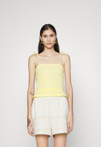 Top cropped amarelo com babados, alças ajustáveis e um volante na bainha. Combinado com calções de padrão leve, exibindo um ajuste relaxado.