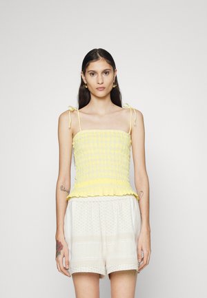 Top cropped amarelo com babados, alças ajustáveis e um volante na bainha. Combinado com calções de padrão leve, exibindo um ajuste relaxado.