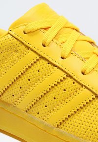 Zapatillas deportivas amarillas con un upper de cuero texturizado, perforaciones circulares, rayas en tono y cordones a juego. Presenta una capucha de talón moldeada.