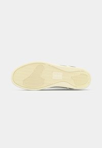 Semelle de sneaker avec une surface en caoutchouc texturé à motif en chevron, semelle intermédiaire couleur crème et un détail de logo en relief.