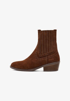 Bottine en suède marron avec une forme effilée, des coutures verticales et des perforations sur les côtés. Présente un petit talon empilé.