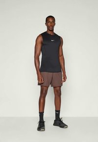Čierny športový top bez rukávov, hnedé šortky, čierne tenisky. Top má malú bielu značku Nike; outfit je priliehavý a funkčný.