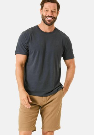 Dunkelblaues Baumwoll-T-Shirt mit kurzen Ärmeln, rundem Halsausschnitt und dezentem Logo auf der Brust, kombiniert mit hellbraunen Shorts, lässige Passform.