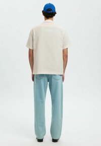 Lichtgekleurde, kortärmelige, geblokte blouse met een ontspannen pasvorm, gecombineerd met lichtblauwe, ruime jeans en een blauwe pet.