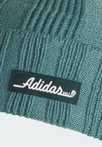 Bonnet tricoté en teal avec une texture côtelée. Présente une étiquette noire brodée avec "Adidas GOLF" en blanc et une icône de golf.