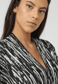 Cárdigan de punto en blanco y negro con un patrón abstracto texturizado, que presenta un diseño de escote en V profundo y finos detalles a lo largo de los bordes.