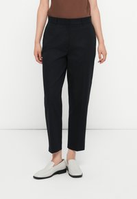Fekete, egyenes lábú, szabott nadrág, sima elülső résszel. Világosszürke slip-on cipővel és barna felsővel párosítva.