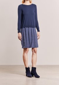 Haut tricot bleu marine à encolure ronde, associé à une robe bleu marine et blanche à motif avec une taille élastique, et des bottines bleu marine.