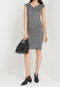 Robe ajustée à carreaux gris avec des manches courtes et un décolleté en forme de trou de serrure, associée à des bottines en cuir noires et à un sac à main structuré.
