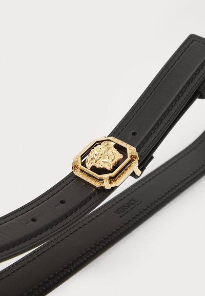 Juodas odinis diržas su auksiniu aštuonkampiu liūto galvos sagtimi, pasižymintis sudėtingais ornamentais ir lygiu paviršiumi. Yra Versace ženklas.