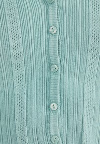 Ljusblå stickad kofta med vertikala ribbningar, texturerade detaljer och sex matchande knappar fram.