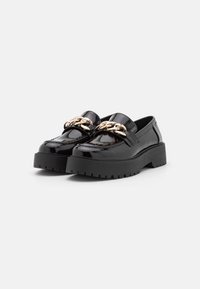 Zwarte gepatineerde leren loafers met een dikke zwarte plateauzool en een gouden kettingaccent over de bovenkant. Gladde textuur en strak design.