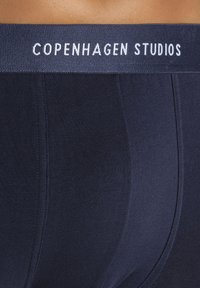 Navy blue boxer briefs with a soft elastic waistband featuring "Copenhagen Studios" in white lettering and a sleek, smooth texture.