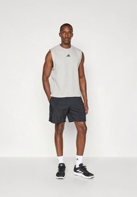 Sportovní outfit zahrnující světle šedé tílko s černým logem, doplněné černými šortkami a černými sportovními botami s bílými detaily.