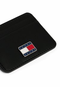 Portafoglio in pelle nera con slot per più carte e un logo metallico brandizzato con sezioni blu, rosse e bianche. Dettagli di cucitura lungo i bordi.