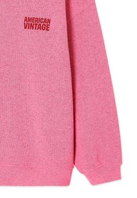 Sweat-shirt rose à manches longues avec le texte rouge "AMERICAN VINTAGE" imprimé sur la partie supérieure gauche de la poitrine.