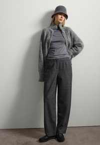 Cardigan en laine gris avec un col, t-shirt gris ajusté et pantalon ample à carreaux gris. Chaussures noires et un chapeau seau en feutre gris assorti.