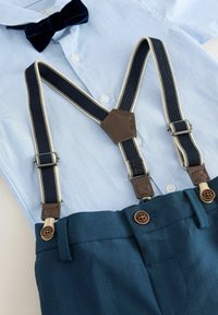 Chemise bleu clair à boutons avec nœud papillon bleu marine, pantalon bleu marine et bretelles bleu marine avec des bords crème et des accents en cuir marron.