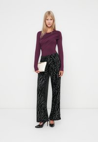 Un body violet profond avec des détails drapés, associé à un pantalon noir taille haute orné d'un motif en feuille d'argent texturé. Tient une petite pochette crème.