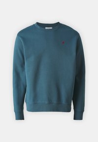 Teal crewneck sweatshirt laget av myk bomullsblanding. Har ribbeformede ermer og nederkant, med en liten rød brodert logo på brystet.