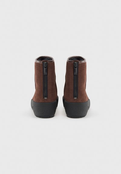 Bottines en daim marron avec semelles en caoutchouc noires et fermetures éclair à l'arrière, dotées d'une doublure intérieure douce et d'un design à bout rond.