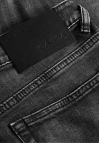 Mörkgrå denimjeans med en svart läderbakpatch som har präglad logotyp. Synliga sömmar längs fickorna och midjebandet.