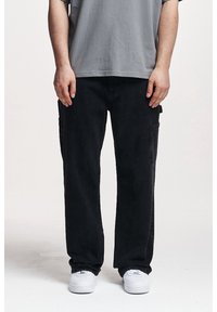 Czarne spodnie cargo wykonane z denimu, z bocznymi kieszeniami i luźnym fasonem. W zestawieniu z szarym t-shirtem z krótkim rękawem i białymi trampkami.