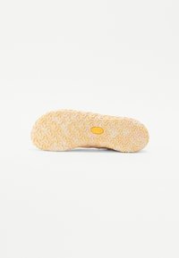 Suela de un zapato con un patrón ondulado y texturizado en color beige claro, que presenta un logo circular en el centro y un acabado ligeramente translúcido.