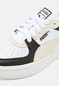 Bílé, černé a krémové kožené tenisky s perforovanou špičkou, bílými tkaničkami a texturovanými akcenty. Obsahují logo Puma na boku a na jazyku.