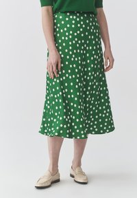 Jupe midi verte à pois, fabriquée dans un tissu léger, présentant de grands pois blancs, une silhouette fluide et un ourlet qui tombe sous le genou.