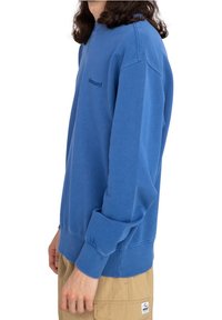 Sweat-shirt bleu avec un col rond, des poignets et un ourlet côtelés. Présente un logo discret brodé sur la poitrine. Tissu en coton doux.