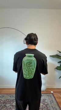 Juodas marškinėliai su dideliu žaliu grafiniu inde su drakono dizainu ant nugaros, demonstruojančiu sudėtingas detales ir raštus.