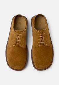 Scarpe in suede marrone con lacci e punta tonda, caratterizzate da una suola in gomma liscia e cuciture ben in evidenza per un tocco di dettaglio.