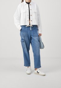 Vit kort jacka med knappstängning, två bröstfickor; blå denim cargobyxor med dragsko i midjan, sidofickor och avslappnad passform; vita sneakers.