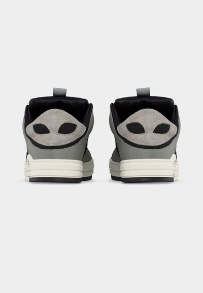 Ζεύγος γκρι και μαύρων αθλητικών παπουτσιών που φαίνονται από πίσω, με λευκές σόλες και γκρι σουέντ επιφάνειες στα τακούνια που μοιάζουν με πρόσωπα εξωγήινων.