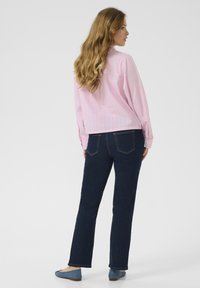 Camicia a righe rosa chiaro con maniche lunghe, abbinata a jeans dritti blu scuro e ballerine blu, vista da dietro.