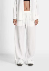 Witte, gestructureerde, wijde broek met een elastische tailleband en trekkoord. Gecombineerd met een losse, witte overhemd met knopen.