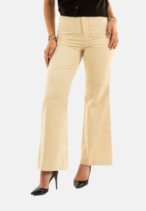 Pantalones de campana de corduroy beige de talle alto, con bolsillos estructurados y una superficie texturizada. Combinados con zapatos de tacón negro.