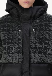 Padded jacket featuring a textured black and gray patterned upper with a smooth black lower section. Includes a high collar and drawstring adjustments.