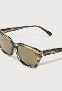 Τετράγωνα γυαλιά ηλίου με διαφανές πλαίσιο σε ελαιόχρωμο πράσινο, καφέ φακούς και μαύρους βραχίονες με χρυσές λεπτομέρειες και λογότυπο.