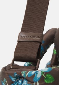 Brun tygrem med en texturerad yta och en läderlogotyp från Marc O'Polo, fäst vid en vadderad del med blommönster.