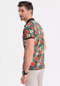 Blommig pikétröja med grön bas, prydd med stora röda och vita hibiskusmönster. Svart krage och ärmkanter. Mjuk tyg.