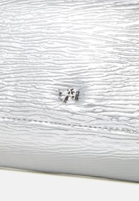 Srebrna torebka o teksturowej powierzchni, z wyraźnym wytłoczonym logo i kontrastującymi detalami szwów.