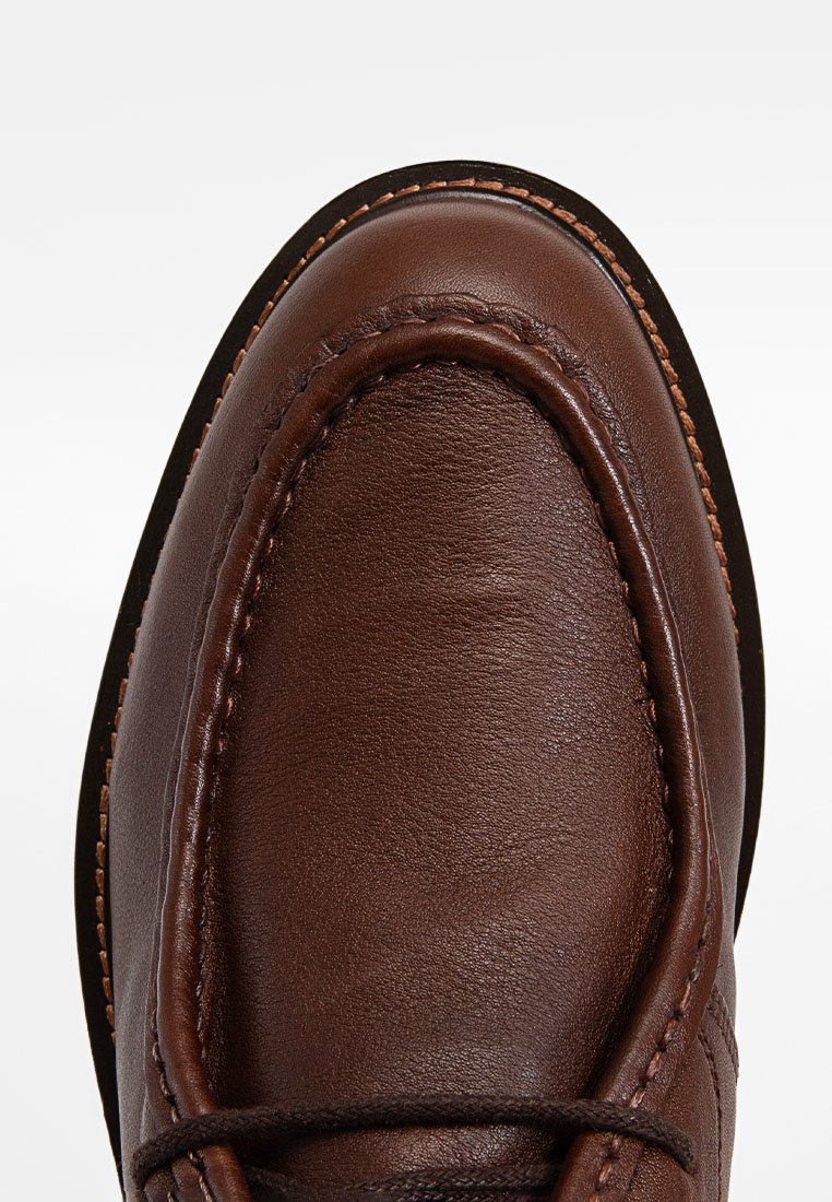 Scarpa in pelle marrone con punta rotonda, cuciture visibili e una texture liscia. Accentuata da un sottile lacci.